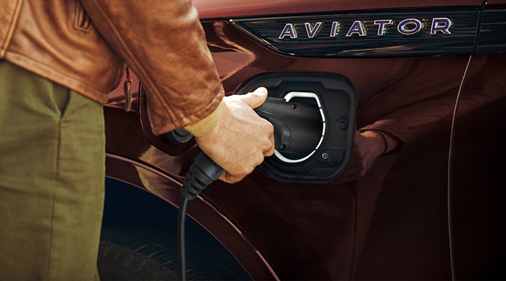 A hand is shown plugging a charger into the charging port of a 2023 Lincoln Aviator® Plug-in Hybrid model. | Rydell Lincoln in Independence IA