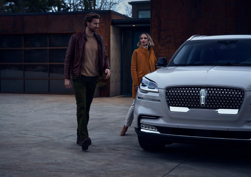A man and a woman approaching a 2024 Lincoln Aviator® SUV, which illuminates certain lights when they are close | Rydell Lincoln in Independence IA