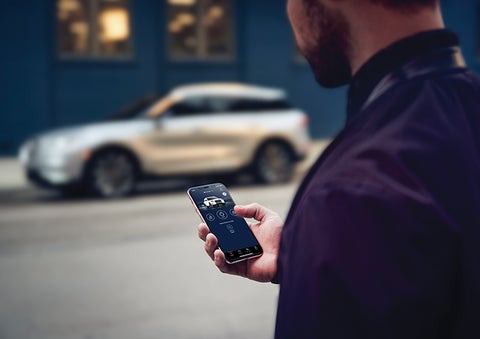 A person is shown interacting with a smartphone to connect to a Lincoln vehicle across the street. | Rydell Lincoln in Independence IA