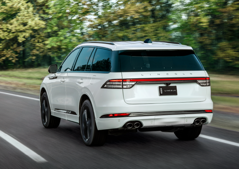 A white 2025 Lincoln Aviator® SUV is being driven away down a road lined with colorful trees. | Rydell Lincoln in Independence IA