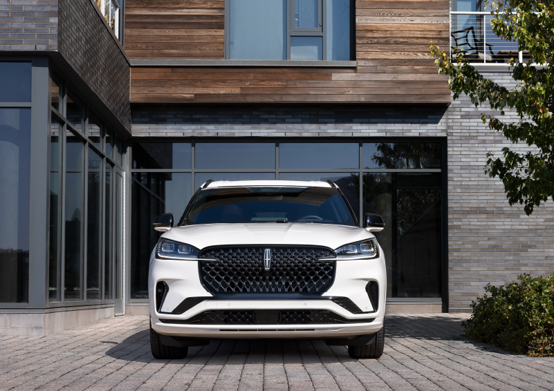 A white 2025 Lincoln Aviator® SUV is shown parked outside a modern building with gray brick and wood accents. | Rydell Lincoln in Independence IA