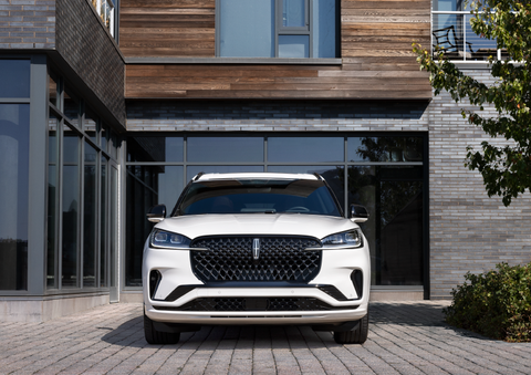 A white 2025 Lincoln Aviator® SUV is shown parked outside a modern building with gray brick and wood accents. | Rydell Lincoln in Independence IA