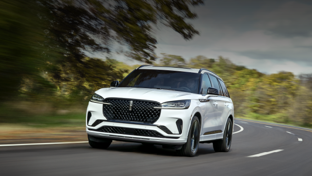 A white 2025 Lincoln Aviator® SUV is being driven down a road lined with trees. | Rydell Lincoln in Independence IA