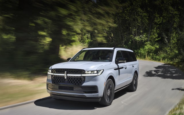 A 2025 Lincoln Navigator® SUV is being driven on a country road.