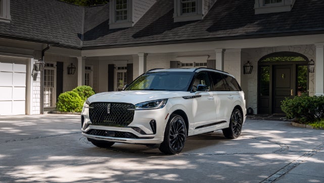 A white 2026 Lincoln Aviator® SUV is parked in the driveway of a luxury home. | Rydell Lincoln in Independence IA