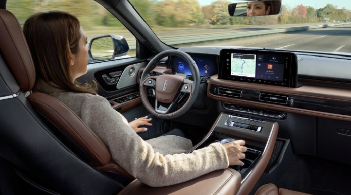 A 2027 Lincoln Aviator® SUV is being driven hands-free on a highway lined with trees. | Rydell Lincoln in Independence IA
