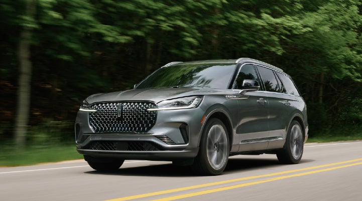 A 2027 Lincoln Aviator® SUV is being driven down a road lined with trees. | Rydell Lincoln in Independence IA
